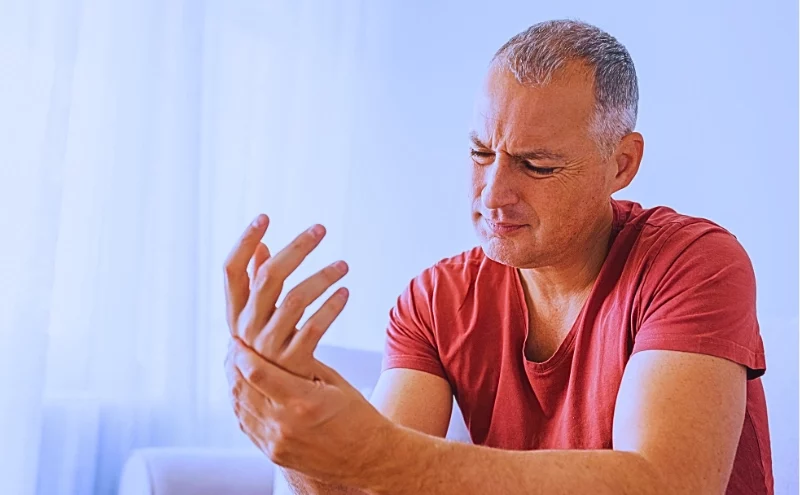 Man suffering from wrist pain at home while sittin on sofa during the day.