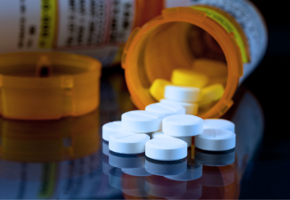 Pills of an opioid abuser spilled onto a table with another pill bottle in the background.